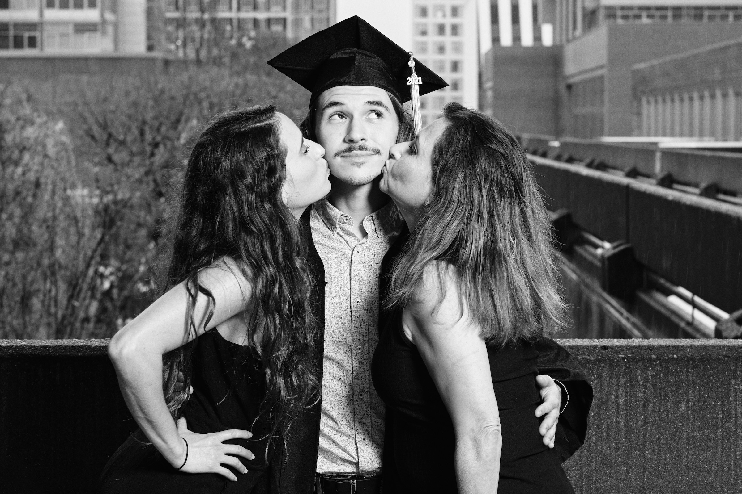 College graduate in cap and gown celebrated with kisses from family