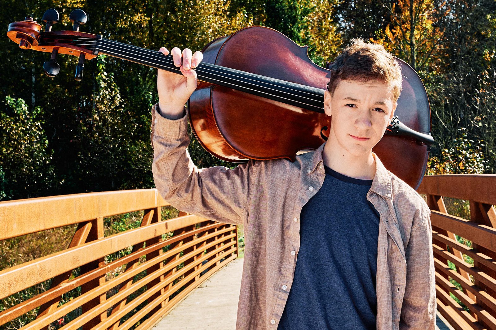 teen male with a cello over his shoulders posing outdoors